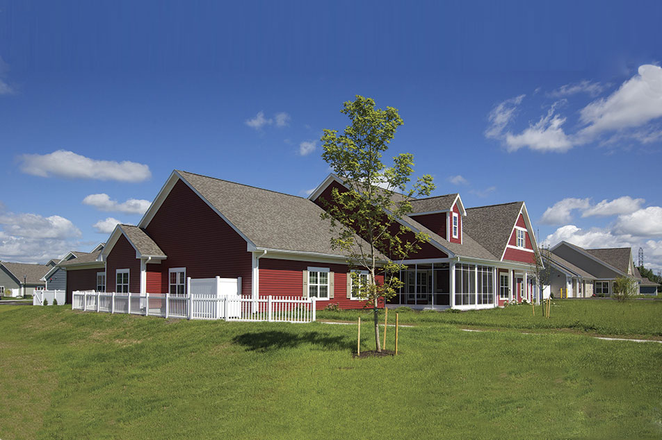 Several cottages with red and grey siding along a green lawn
