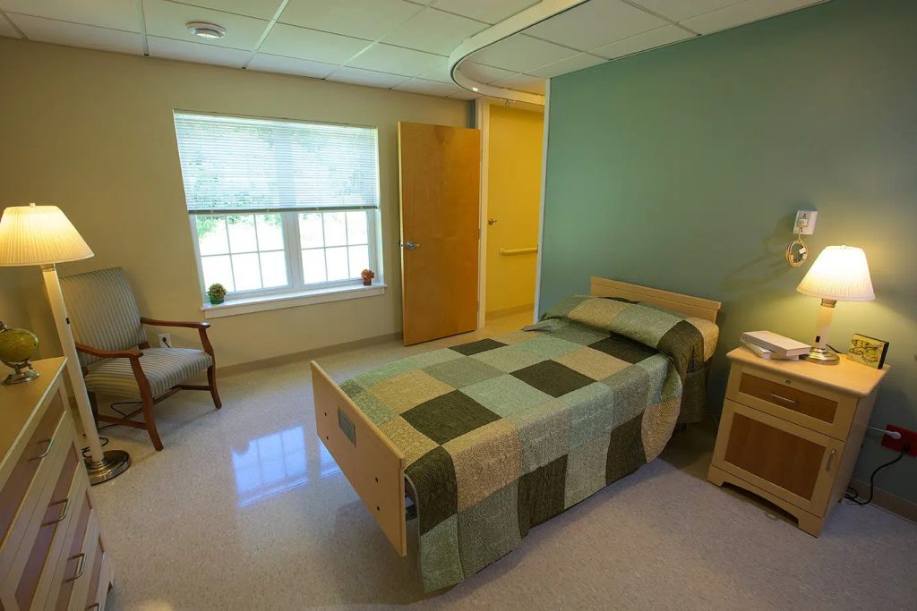 A private bedroom with a quilted bed, nightstand and large window