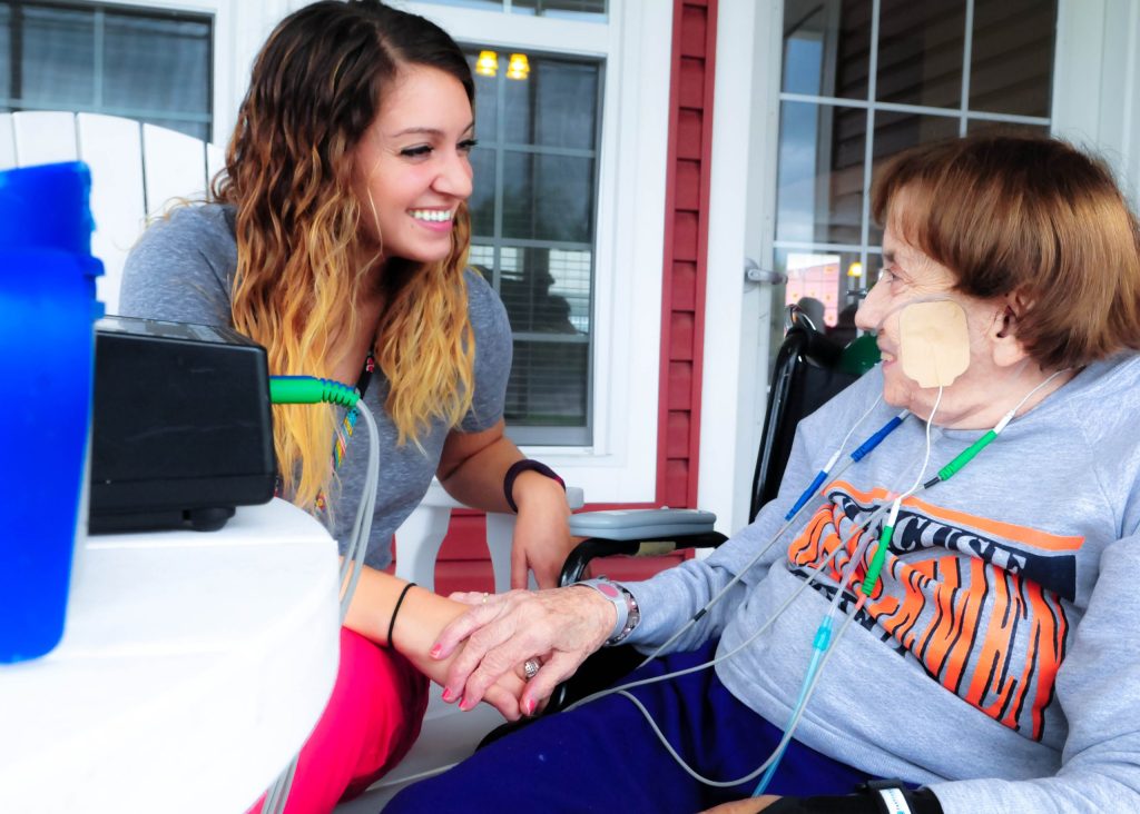 A smiling caregiver holding hands with a resident on a porch